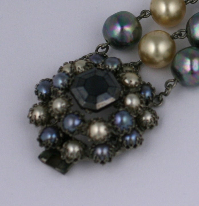 Raro bracciale di Countess Cis composto da tre fili di grandi perle iridescenti grigie e crema firmate a mano da Cis. La grande chiusura è costituita da perle più piccole con incastonatura a griffe, con al centro una pietra quadrata di ematite