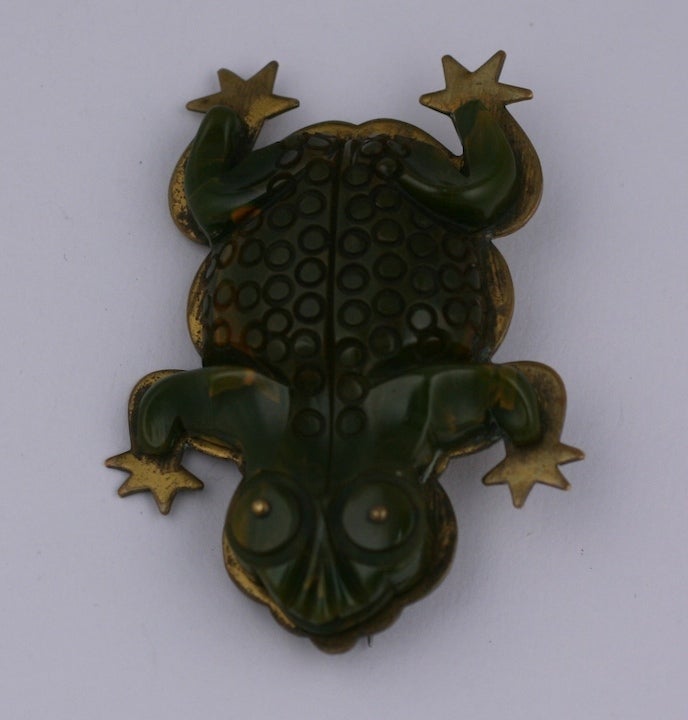 Charming art deco bakelite frog brooch backed on a brass backing. Greenish end of day bakelite is carved and incised with froggy detailing and accented with brass ball eyes. 1930's USA.  2.5
