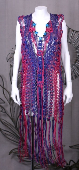 Striking and unusual hand crafted macrame vest from the 1970's. Made of nylon wrapped cording in fuschia and purple tones with Chinese knots and faience beads intertwined. 2 side knot closures on each side. Originally worn over a purple spandex cat