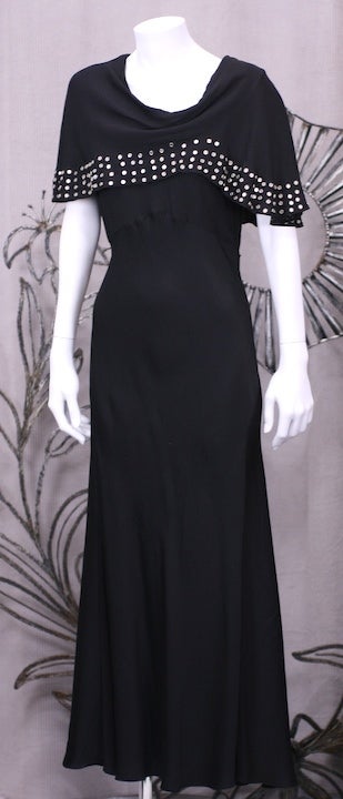 Unusual gown from the 1930's with metal stud detailing. A precursor of punk style, the detailing on this rayon crepe gown is as innovative as the off kilter side draped cowl neckline. 
Gowns from the period like these which are incredibly modern