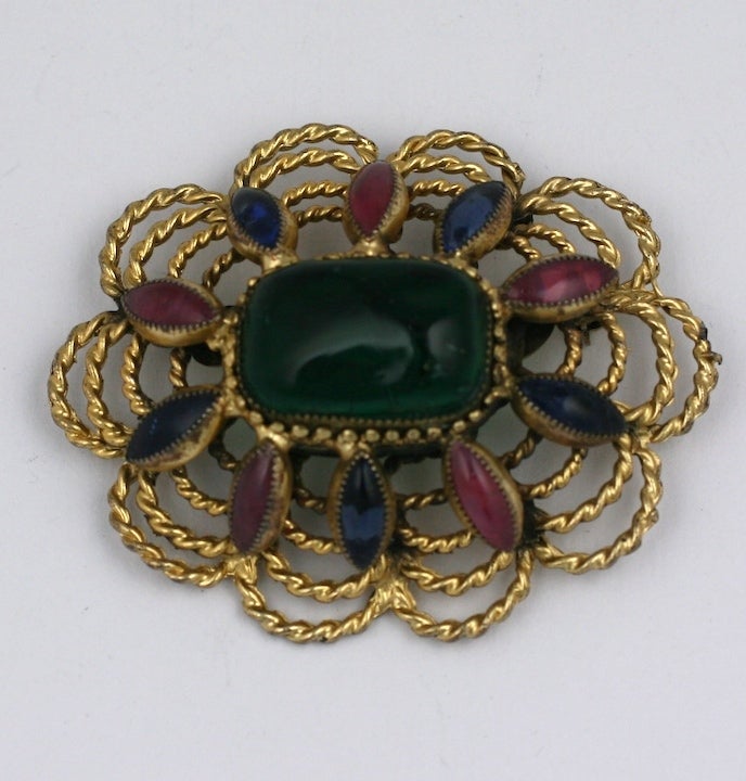 Hattie Carnegie poured glass oval brooch produced Maison Gripoix by  Gripoix, France. Gilt metal is twisted to form the crest shaped brooch with large emerald glass cab center. 1950's USA.
3.25