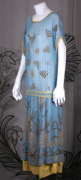 1920s cotton muslin day dress in pale blue with Japonesque embroideries and beadwork. Trimmed in pale yellow piping with crysanthemum motifs beaded along the hem with silk floss embroidered leaves.  
The House of Adair produced unique beaded gowns