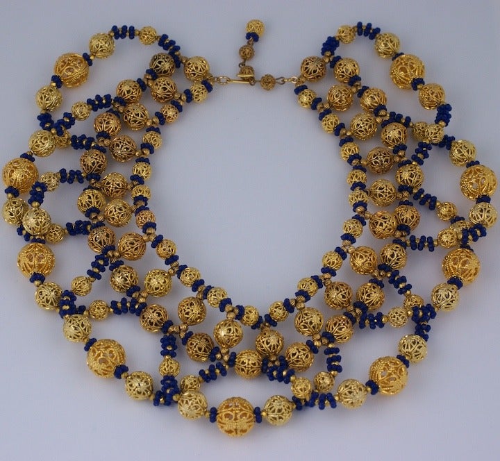 Large collar composed of gilt filigree balls and deep blue pate de verre spacers and gilt beads. Large loops of beads emanate from the central strand on neck. 1960's USA.
Adjusts from 13.5