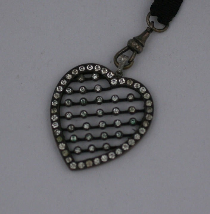 Edwardian Paste Pierced Heart Pendant swivel mounted on a long silk grosgrain ribbon lariat with slide.  Silvered metal with glass paste stones. 1900's USA. 
44