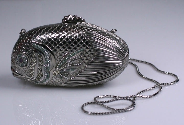 Silvertoned Jeweled fish minaudiere by Judith Leiber with retractable shoulder strap and comb. Pave stones are in aqua, smoke and crystal with genuine amythest cabochon pupils in the eyes on both sides. Realistic detailing with the tail curling back