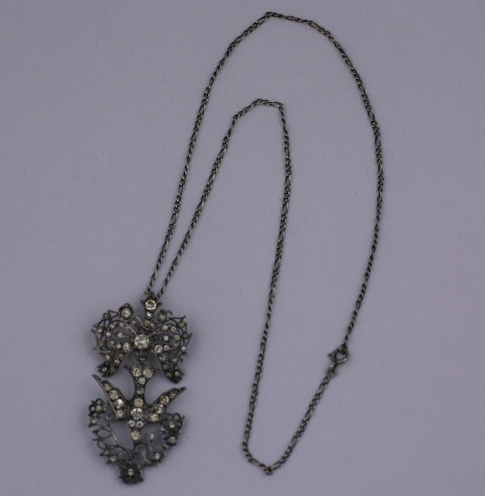 Paste French bird pendant from the early part of the 19th Century. Paste stones are set throughout the sterling model. A bird hangs from an ornate bow clutching flower sprays in its beak. Chain 18