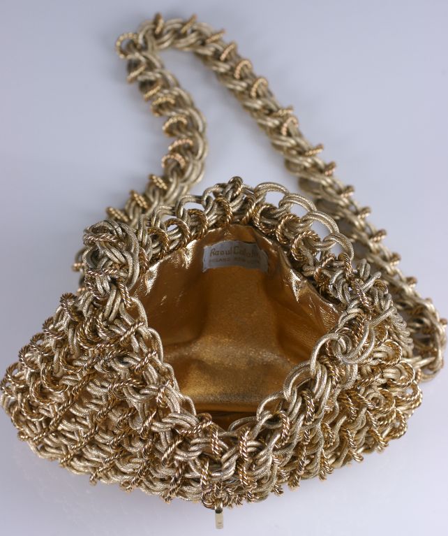 Gilt chain mail shoulder bag made from a combination of matte gold chain links and high polish gold twisted jump rings. Ornate handmade construction. Chain link strap and hook keeps bag closed. Lined in gold leather. Weighty quality piece.<br