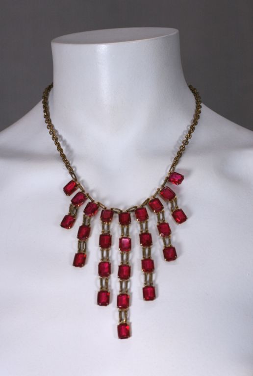Unusually proportioned Czech necklace from the 1920s. Faceted emerald cut stones in ruby glass are suspended in a bib formation. Ruby stone in clasp as well. Metal is brass finish.Large and striking scale.<br />
15