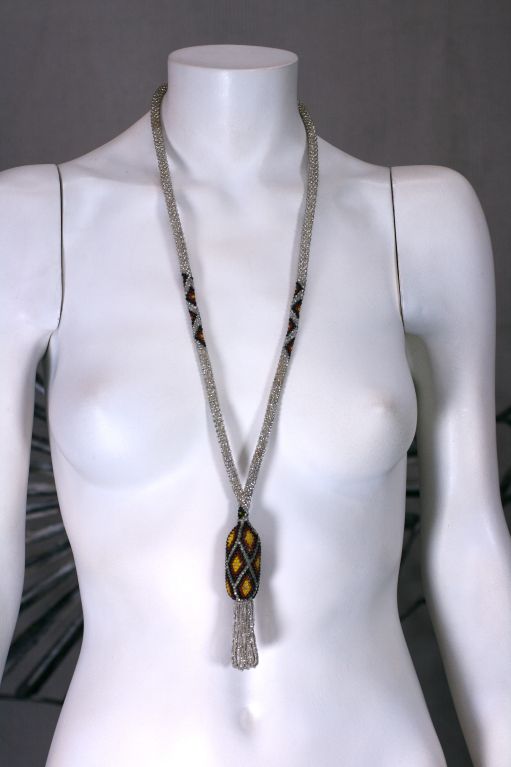Striking deco hand beaded necklace of patinaed silvered beads with ruby, black and yellow accents. The patterned centerpiece is woven aound a core and a tassel hangs from it.<br />
30