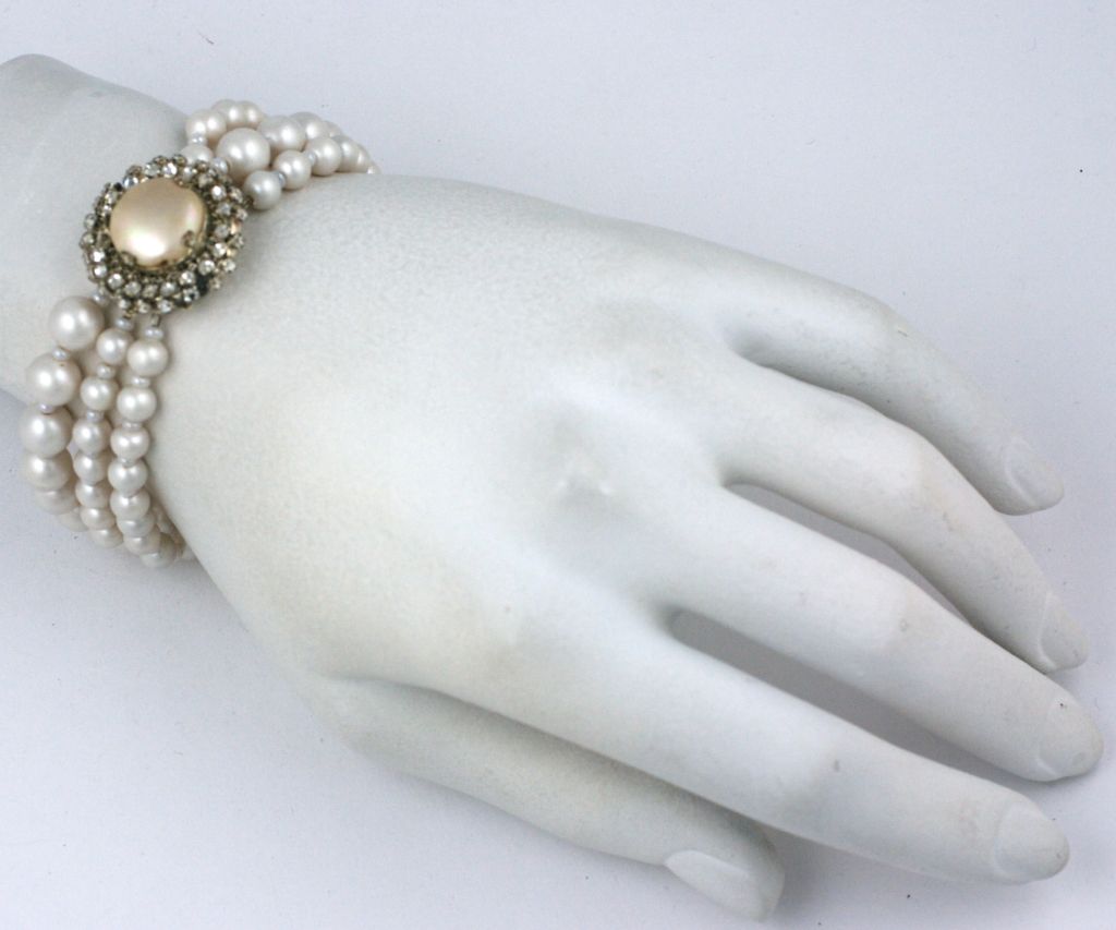 Bracelet en fausses perles d'eau douce Miriam Haskell à trois brins, dont le fermoir est une perle bouton irisée décorée de rosettes cousues à la main.<br />
Excellent état<br />
Longueur : 8