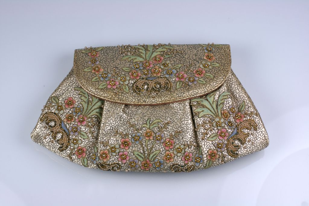 Lovely silk satin clutch which is rembroidered with metallic threads, floral sprays, beads and pearls. The edges are piped in gold kid leather.<br />
Can be used with bow handle or worn as a clutch. Lined in pink rayon satin. <br />
10 x 7