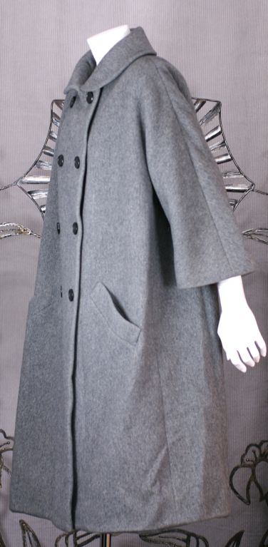 Élégant manteau A-line en laine flanelle grise de Norman Norell. Fermeture à double boutonnage avec doublure en soie taupe. Construction de haute qualité avec des boutonnières reliées et des manches kimono 3/4 à soufflet.<br />
Poitrine : 46