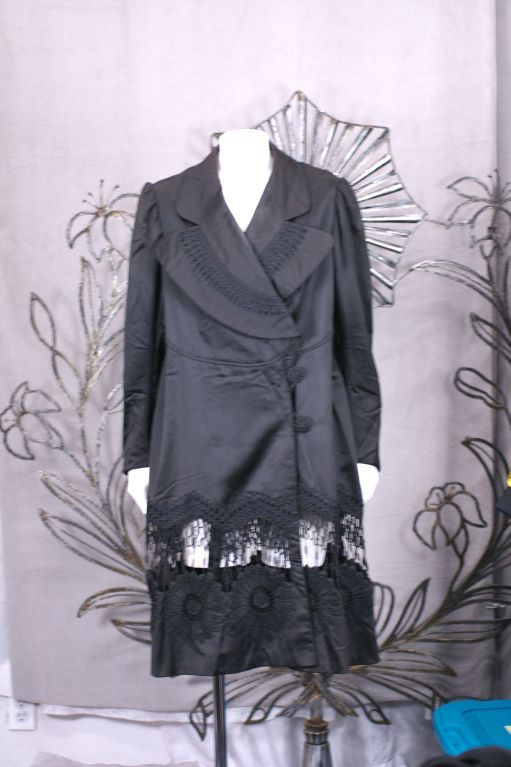 Unusual European walking coat from the late 19th/early 20th Century. Black cotton sateen is tailored with black passementerie and embroidery. A panel of passementerie openwork is attached below the hip line to reveal openwork attached to sunflower