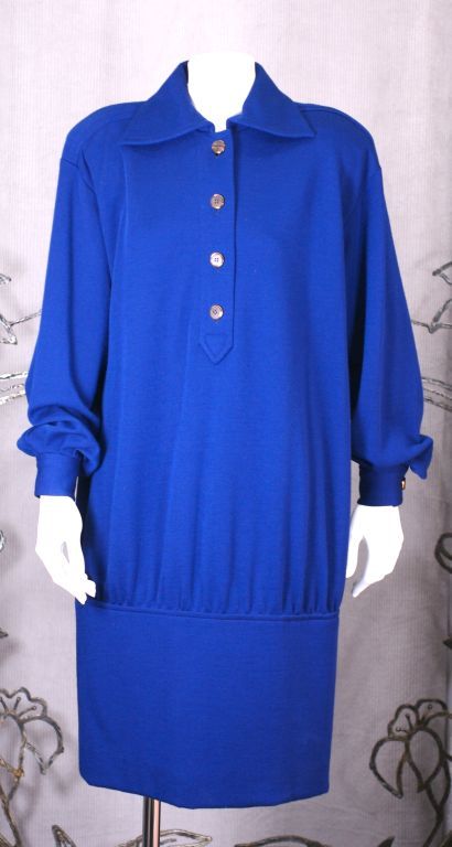 Classic Yves Saint Laurent wool jersey tunic dress in electric blue with gold buttoned placket. Bold shoulder line and shirt detailing rendered by YSL into its most feminine form. 1980s. France.<br />
