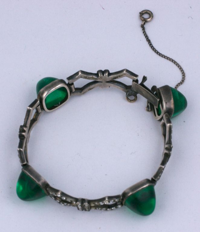 Elegant art deco paste bracelet set in sterling with large faux emerald bullet cab stones. Pierced articulted metalwork in art deco bow motifs.<br />
Excellent