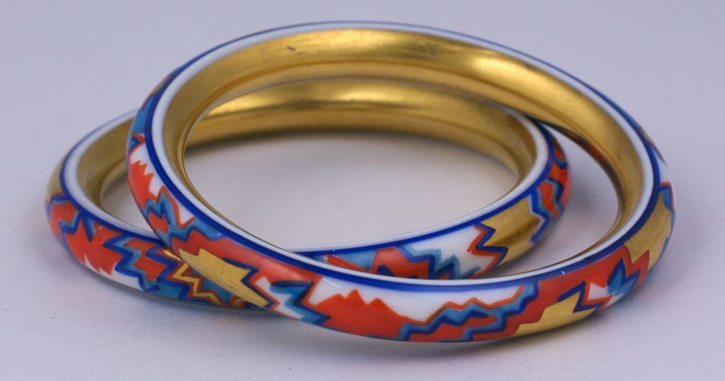 Unusual pair of unusual porcelain bangles hand decorated with deco zig zag patterns of gold leaf with reds and blues. Each bangle is entirely gilded on the interior as well. European circa 1930s.<br />
Excellent unworn condition.