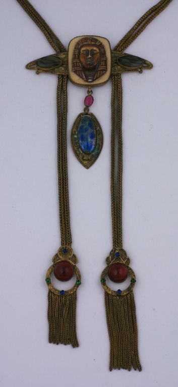 Unusual and collectible eygptian revival necklace from the 1920s. Gilded brass with unusual czech glass stones throughout. A celluloid molded pharoah's head forms the centerpiece. A pair of gilt jewelled "tassels" falls from the pharoah