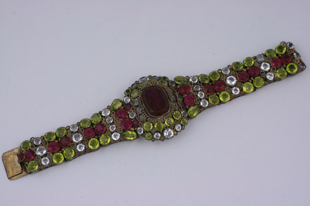 Elaborate Hobe bracelet from the 1930s with ruby, chartreuse and clear open back crystals set into an intricate filigreed frame. Each stone is bezel set and embellished with looped wirework. A large ruby crystal forms the centrepiece of this