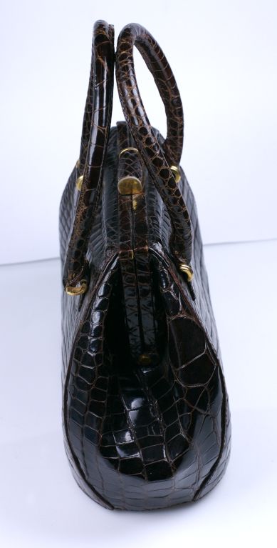 Amazing center cut alligator bag in deep chestnut brown in an unusual yet modern shape. Dimensional bag has skin covered toggle and padded handles. All hardware is gilded gold with tiny ball feet on the base. Completely lined with zippered pockets