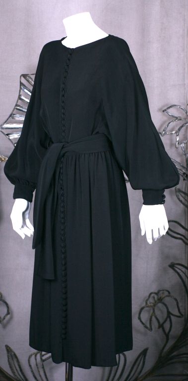 Simple and easy heavy weight crepe dress by Donald Brooks with dozens of covered buttons running down the front. Bateau neck with full gathered kimono sleeves and attached self sash. 
One piece with front button closures. Fully silk lined. 