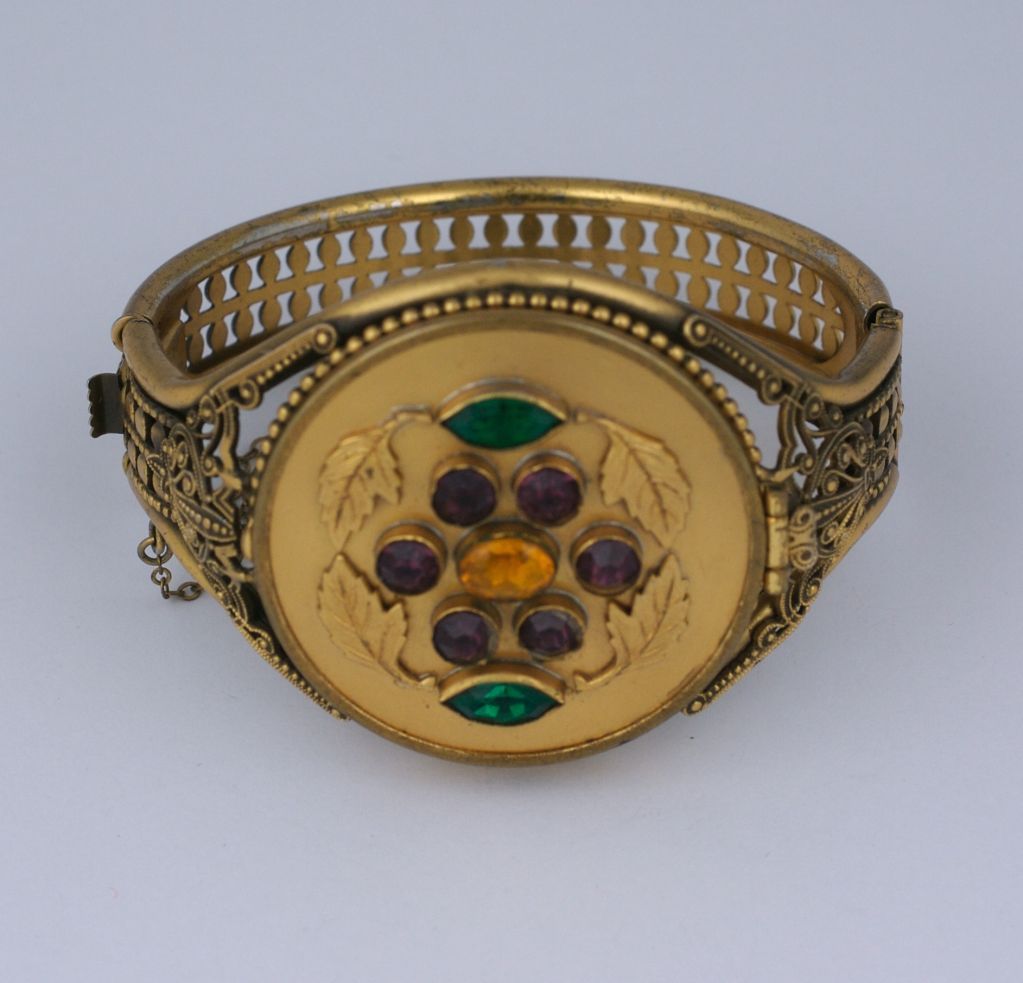 Jewelled cuff with hidden compact and mirror from the 1940s. Bezel set with faux emeralds, amythests and citrines. Filigreed gilt settings with hinged band and safety chain. Mirrored interior. Never be caught unprepared. USA 1940s.
Excellent