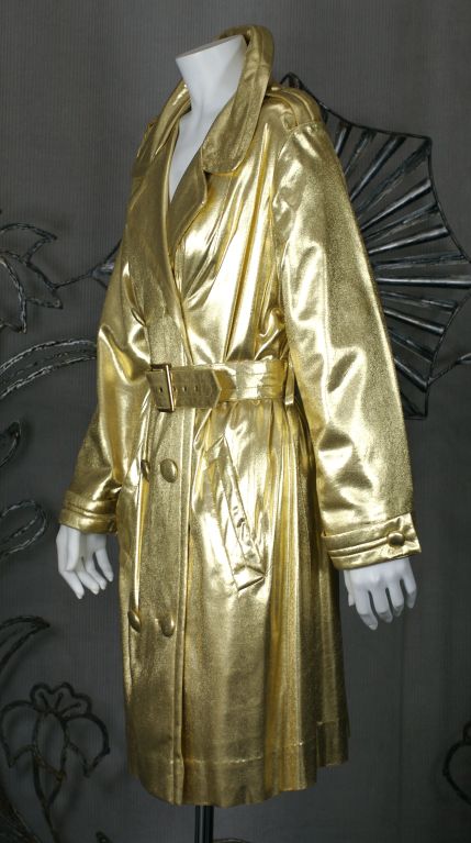 Traditional mini trench in an unusual gilded fabric on a jersey bonded base. Covered buttons with trapuntoed belt and buckle.<br />
Fabric has a liquidy texture that shimmers with every move. Made as an evening coat but can be worn in so many