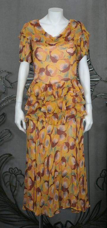 Robe de danse en mousseline de soie imprimée déco des années 1920. Ravissantes fleurs abstraites sur une base de mousseline de soie froissée ocre brûlé, avec des volants à la taille et au cou. Entrée latérale à boutons-pression.<br />Doublure