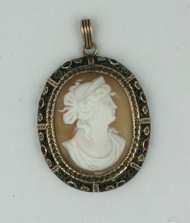 Antique 19th Century shell cameo surrounded in a silver and gold bezel,set with colored stones. Synthetic rubies and sapphires are bezel set around the frame. Lovely gold floral work and borders pop against the darkened silver ground. Elaborate hand