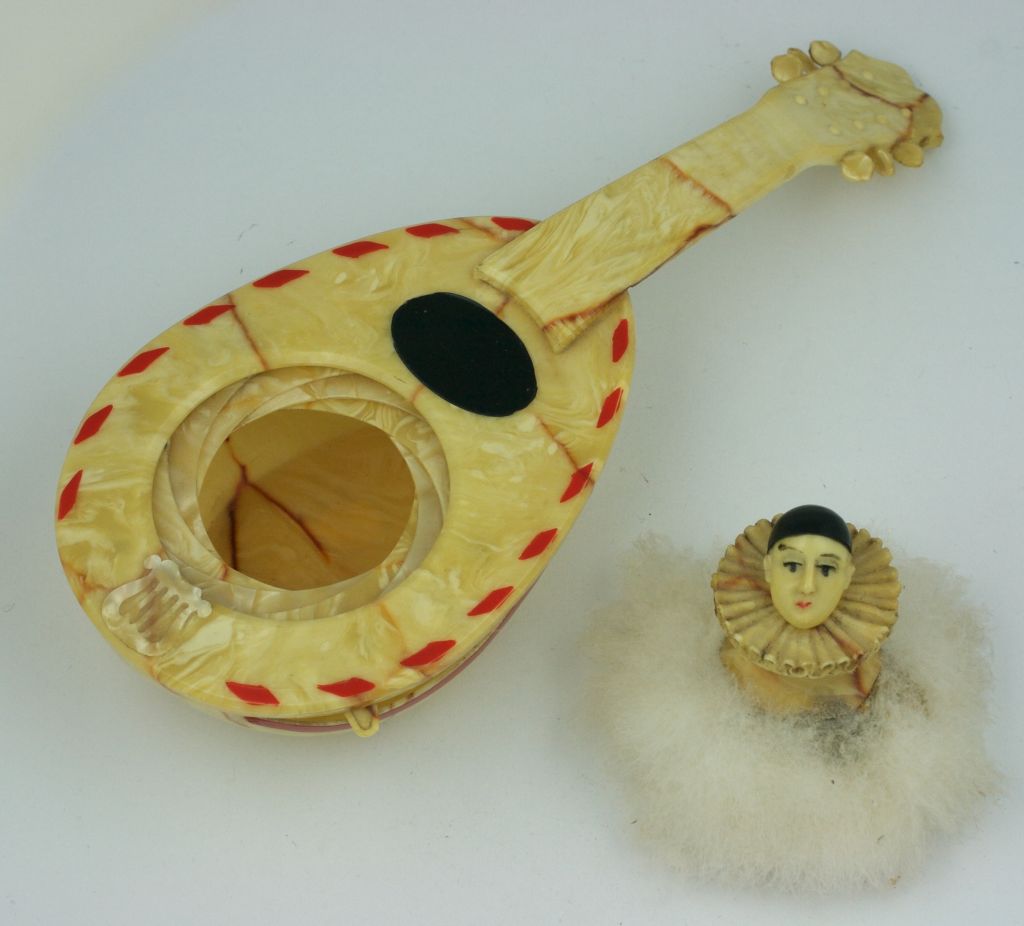 Figural powder puff of Pierrot hidden in a celluloid mandolin.<br />
Pearlized and marbleized celluloid is used for this unusual table piece. Pierrot "puff" is hidden in a retractable door which opens by pulling down a lever along the