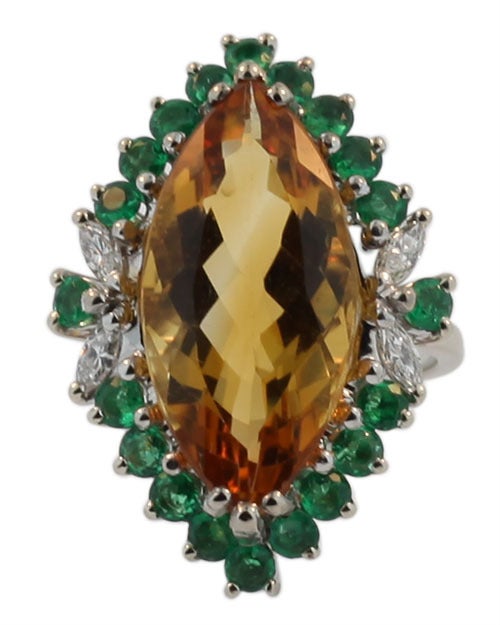 This unique ring is clearly stamped 14 KT. It also bears the makers mark P.H. in a oval cartouche. It contains a large 9.0 cts marquise cut citrine. The citrine is bordered by 20 round lovely green emeralds. Additionally there are 4 marquise cut