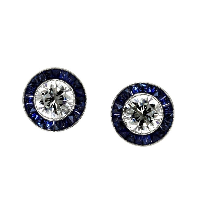 A classic pair of  diamond stud earrings surrounded with sapphires, set in Platinum. The two diamonds are estimated to weigh a total of 3 carats, H color, SI1 clarity. GIA Diamond Certification service available at an additional charge.