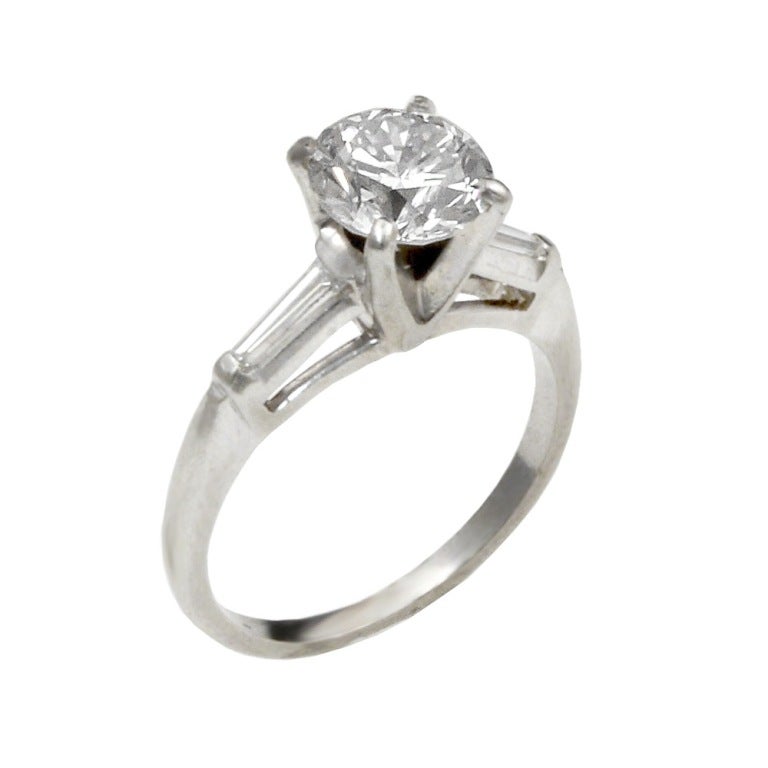 A simple and classic diamond engagement ring with the center stone weighing 1.44 carats, and the side stones approximately 0.20 carats total. The estimated color and clarity of the center round brilliant-cut diamond is I-SI1. The tapered baguettes