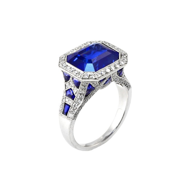 A beautiful and elegant handmade engagement ring centered with a rectangular step-cut sapphire weighing over five carats accented with diamonds and custom-cut sapphire baguettes, set in Platinum. Size 6 1/4 US