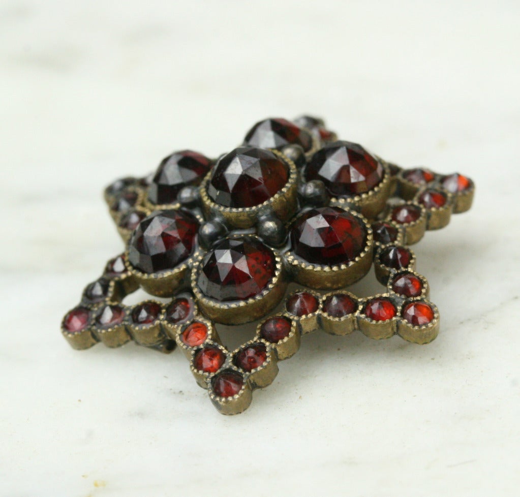 - Brass, rose-cut garnets

Breathtaking rose-cut garnets form a three-dimensional flower cluster at the heart of this star-shaped pendant. Delicate millegrain bezel settings show how expertly and lovingly crafted this lovely antique piece