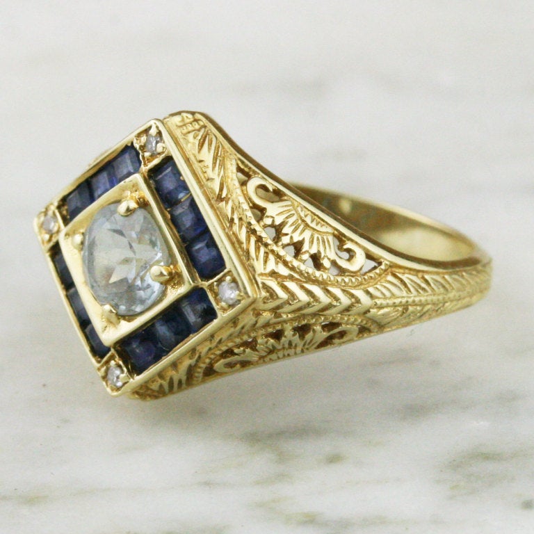 - Filigree Engagement Ring
- c. 1960-1980 *
- 14k yellow gold, one 5 mm round brilliant-cut aquamarine of approximately .4 carats, twelve 1.75 mm square-cut sapphires for a total weight of approximately .24 carats, four approximately .005 carat