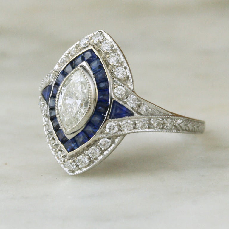 - Diamond and Sapphire Engagement Ring
- 20th century (due to the long-lasting popularity of deco styling, it can be difficult to date pieces in this vein)
- 18k white gold; .7 carat marquise-cut center diamond; 20 square- and triangle-cut natural