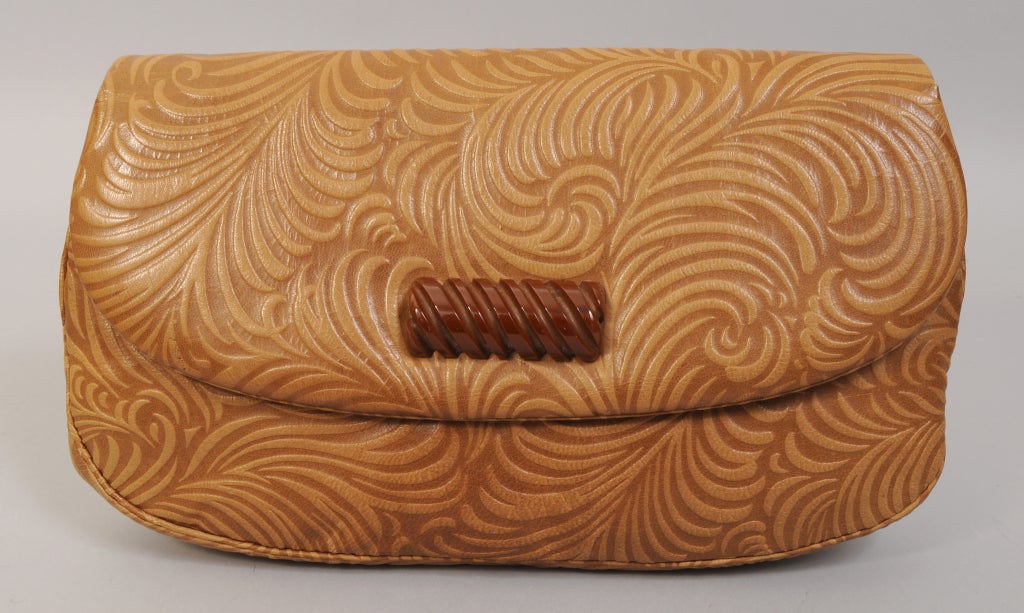 This roomy bag is a tooled leather clutch with feather designs from Jacomo, Paris. It has a vintage bakelite clasp. The bag is lined with brown leather and has two slip pockets, a lipstick pocket and one zippered pocket. It is in excellent