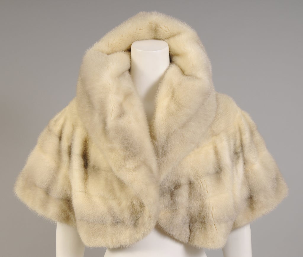 Perfect for a cool evening this cross mink bolero is a flattering cream with grey accents. The jacket has a generous shawl collar, elbow length sleeves, and a floral embroidered lining. This great jacket is from the estate of a Manhattan socialite.