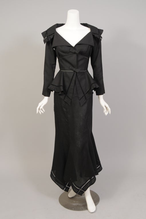 A stunning black linen evening suit from Thierry Mugler has a fabulous low neckline, a fitted jacket and a peplum with a handkerchief hem. The collar, waist and hem are trimmed with open drawn work. The matching skirt is long and lean with a