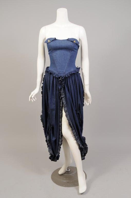 A denim bustier tops a gathered denim skirt in this strapless dress from Moschino. The top is boned for support and has a left side zipper. The skirt has a high slit at the center front. It is gathered and has a ruffle around the hem. It is in