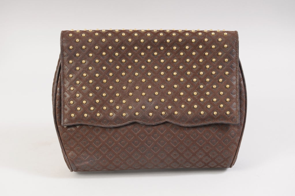 A great day into evening clutch this dark brown leather bag has an unusual lattice design. On the front flap the design is accented with round brass studs in the lattice diamonds. The front flap has a scalloped edge with a hidden snap closure. The