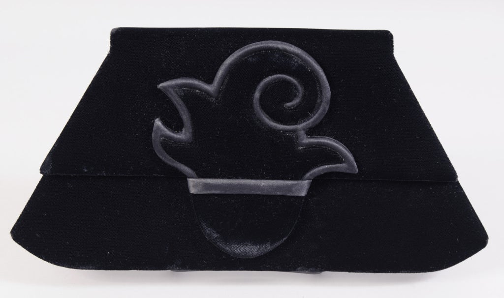 A chic black velvet clutch designed by Paloma Picasso is decorated with a satin edged ornament. The bag is lined in black satin and it has one open pocket inside. There is no shoulder strap. It is in excellent condition.

Measurements;
Height