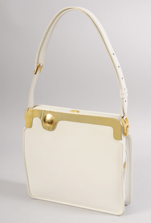 A mint condition mid century bag from Nettie Rosenstein is trimmed with a fabulous brass ornament on the front side. It is a flat piece of metal, cut and curved, with a raised circle on one side. The bag has a convertible strap and it is in pristine