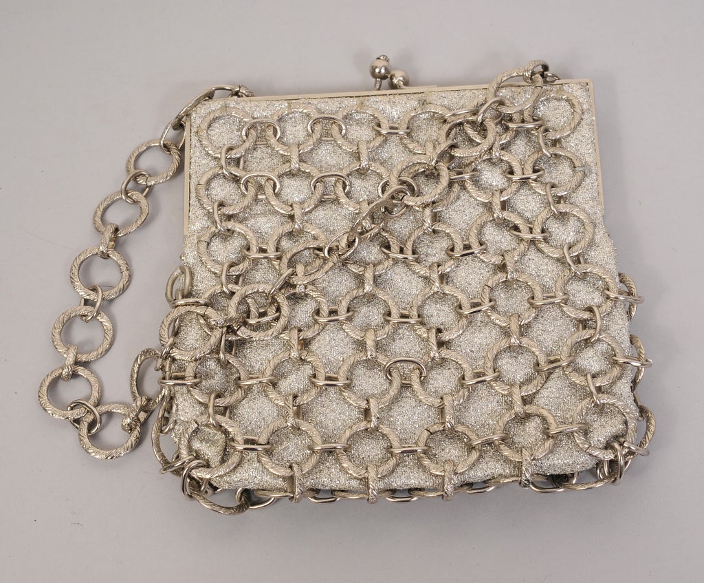 This 1970's evening bag has a metal frame, kiss lock and a silver lame body covered with interlocking silver metal chains. The handle is made from the same chains. The interior of the bag is white satin and it is marked Made in France. This great
