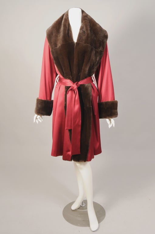 Sheared mink is used for the generous shawl collar and cuffs of this burgundy satin coat designed by Louis Dell'Olio. The coat has a matching tie belt, two pockets, and it is fully lined in deep red silk. It is in pristine condition and appears
