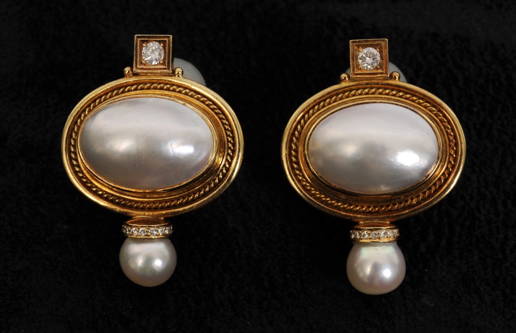 This stunning pair of Vallois earrings from English designer Elizabeth Gage is made from 18k gold, with a diamond in a square at the top. This sits above a large Mabe pearl surrounded by a twisted wire design. Below this there is a circle of
