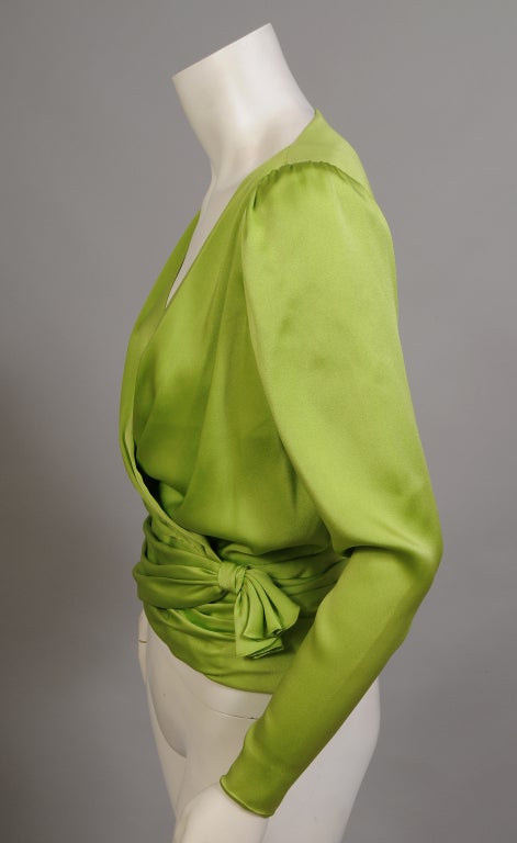 A simple cross over wrap style blouse is made with the most amazing couture construction in the most amazing shade of acid green. The blouse has long narrow sleeves with zippers at the cuffs. The pleated front is attached by a wide cummerbund which