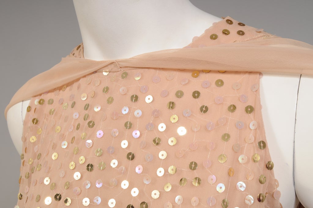 Pale peach chiffon is sprinkled with golden sequins and accented with flowing chiffon panels that can be worn in a variety of ways. The dress has a round neckline, cut in arm holes, and a fitted silhouette through the torso. It is fully lined and it