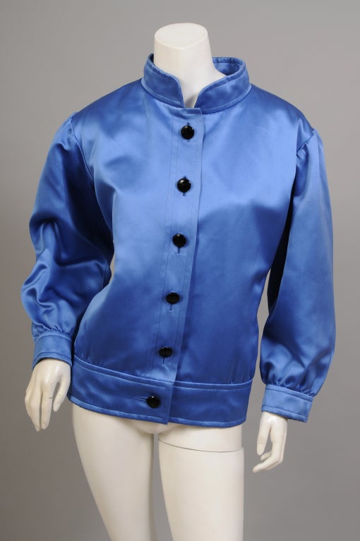 Rich blue silk satin is paired with glittering black jet buttons in this elegant jacket from Yves Saint Laurent Haute Couture. The jacket has a band collar, button front, fitted waist band and matching cuffs. It is cut full through the body and