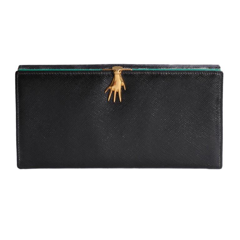 Beautiful and pristine, this charming Gucci wallet is still in the original box. A golden hand clasps the wallet tightly closed on the front. On the back there is a pocket for change. 
The interior has two bright green pockets. One side is marked
